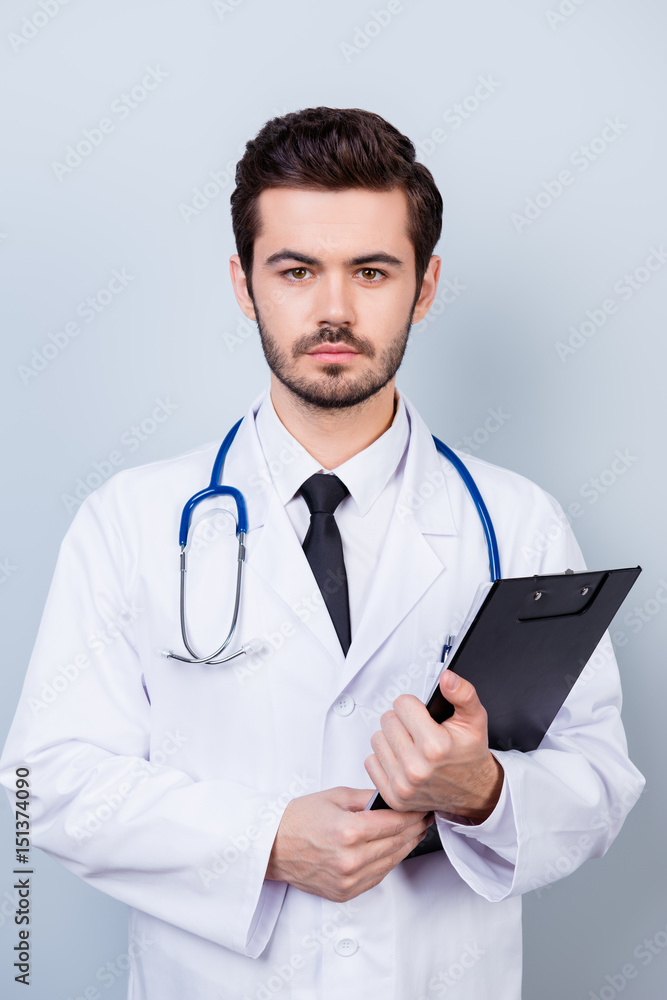 Vertical photo of serious confident bearded doctor with stethoscope and clipboard ready for the consultation Vertical photo of serious confident bearded doctor with stethoscope and clipboard ready for the consultation