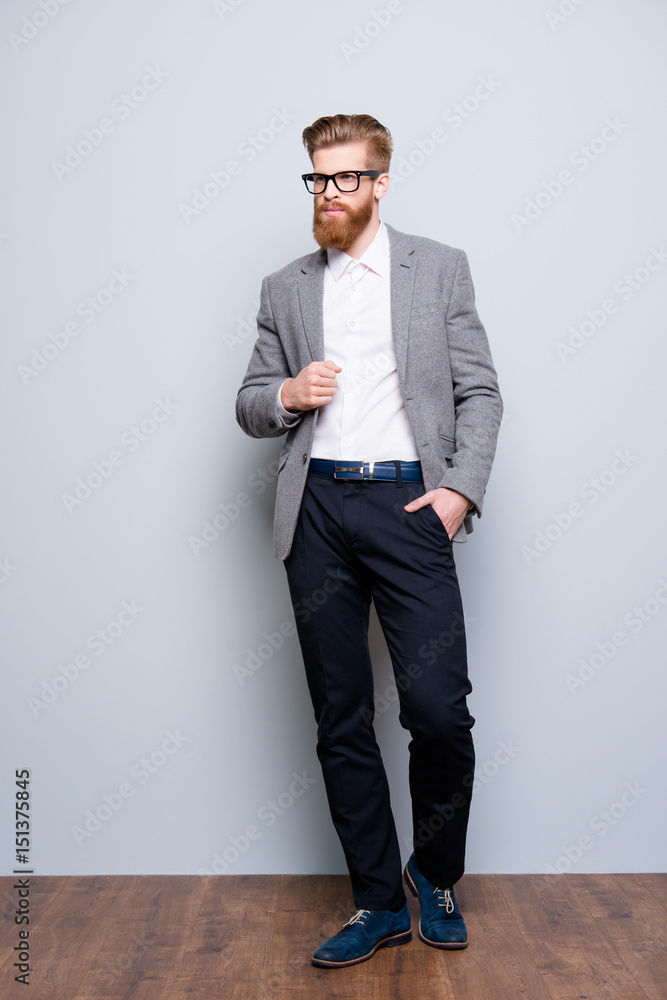 Full size portrait of stylish young bearded man standing on gray background. He looks stunning! in a suit and with glasses Full size portrait of stylish young bearded man standing on gray background. He looks stunning! in a suit and with glasses