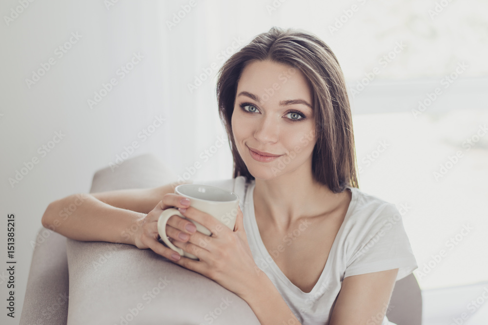 Portrait of pretty young woman sitting on couch and drinking coffee from beige mug Portrait of pretty young woman sitting on couch and drinking coffee from beige mug
