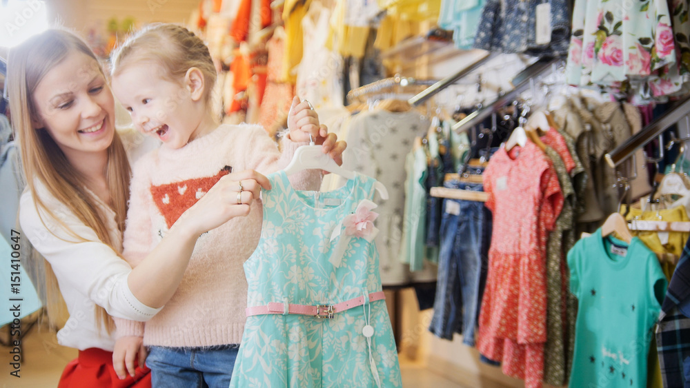Blonde little girl with mother buying sweatshirt - kids clothes in store
