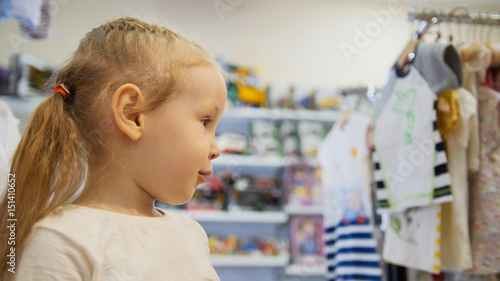 Cute blonde baby girl in child dress store
