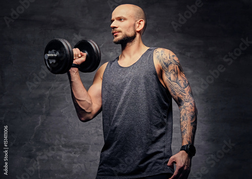 Sporty shaved head tattooed male doing biceps workout with dumbbell.
