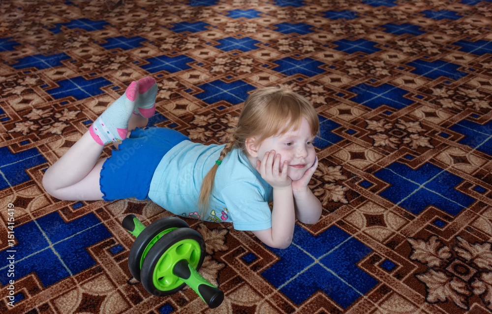 Naklejka premium little girl child is 5 years of playing sports at home itself. He is engaged with the roller, smiling, close-up. Merry training. Healthy lifestyle since childhood.