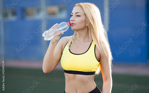 Slim young woman drinking water after training