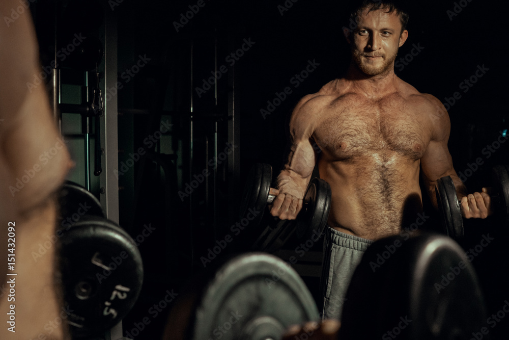 Naklejka premium inflated handsome man raises heavy dumbbells on a black background. fitness. gym.