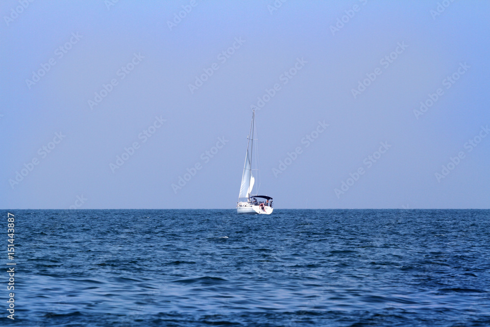 A sailing boat is sailing on the open sea. The sun is shining.