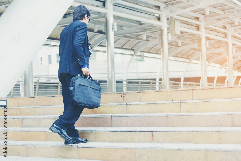 Business man carrying a suitcase and going up the stairs  in the city.