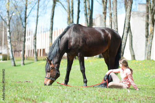 Young teenage girl owner sitting close to her favorite horse