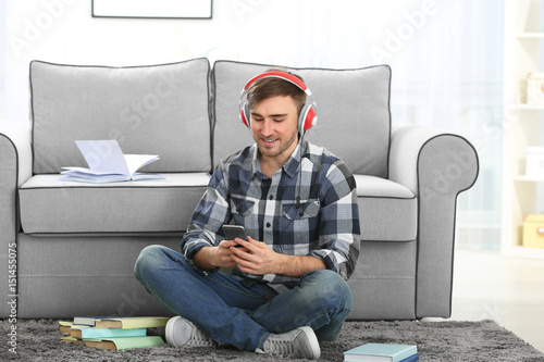 Concept of audiobook. Handsome young man with headphones and phone sitting on carpet at home © Africa Studio