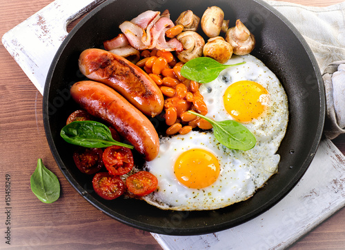 English breakfast in pan with fried eggs, sausages, bacon, beans and mushrooms