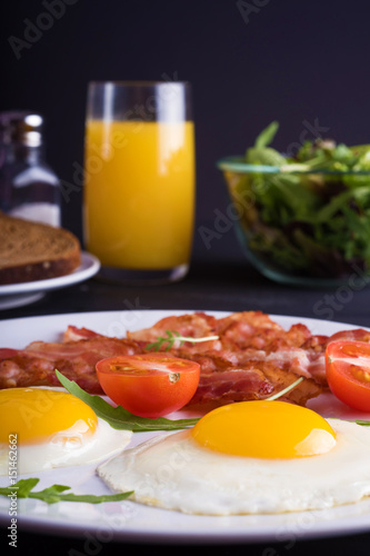 Breakfast with fried eggs and bacon with fresh salad and toast on the table.