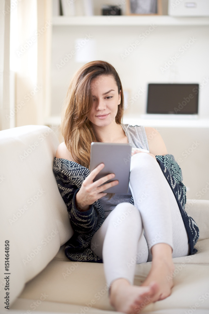 Caucasian girl siting on sofa in the morning and using tablet device Caucasian girl siting on sofa in the morning and using tablet device