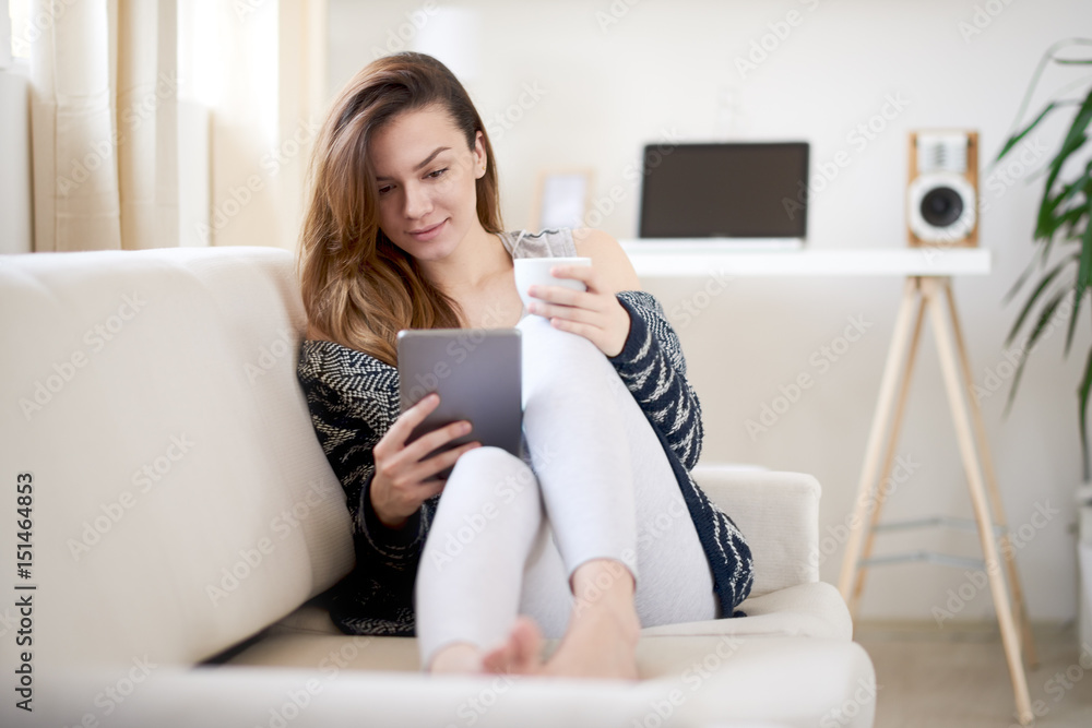 Caucasian girl siting on sofa in the morning and using tablet device Caucasian girl siting on sofa in the morning and using tablet device