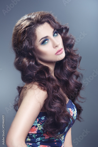 Beauty portrait of a sexy brunette with chic curls isolated on a gray background.