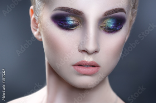 Beauty portrait of a beautiful girl with a bright make-up of peacock coloring isolated on a gray background.