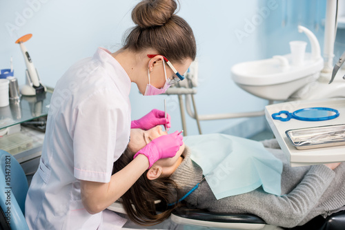 Fotografi Female dentist with dental tools - mirror and probe treating patient teeth at dental clinic office