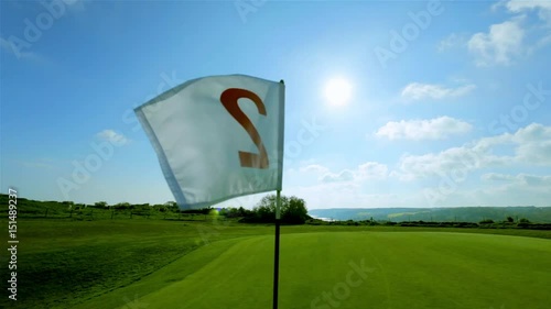 View of a green golf course, hole and flag on a bright sunny day. Sport, relax, recreation and leisure concept. Summer landscape with sunbeams