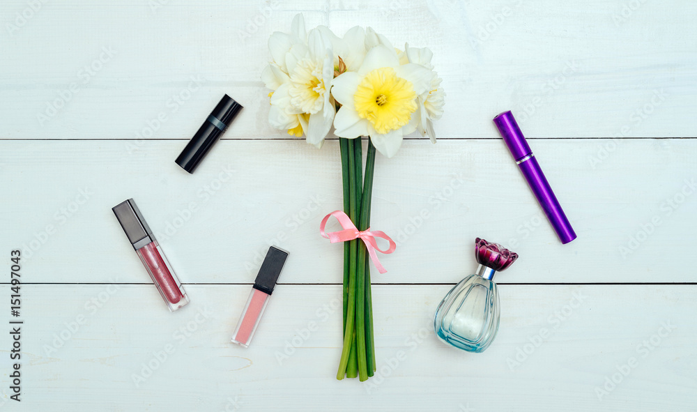 Top view on white wooden background with сosmetics: mascara, lip gloss, lipstick and perfume around bouquet of narcissus. Liquid Lipstick Top view on white wooden background with сosmetics: mascara, lip gloss, lipstick and perfume around bouquet of narcissus. Liquid Lipstick