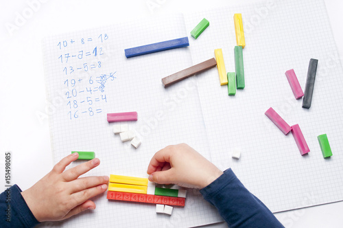 Open exercise book with colored plastic math learning tools number rods on white background. Close-up of children's hands. solving mathematics examples. Educational and school concept.