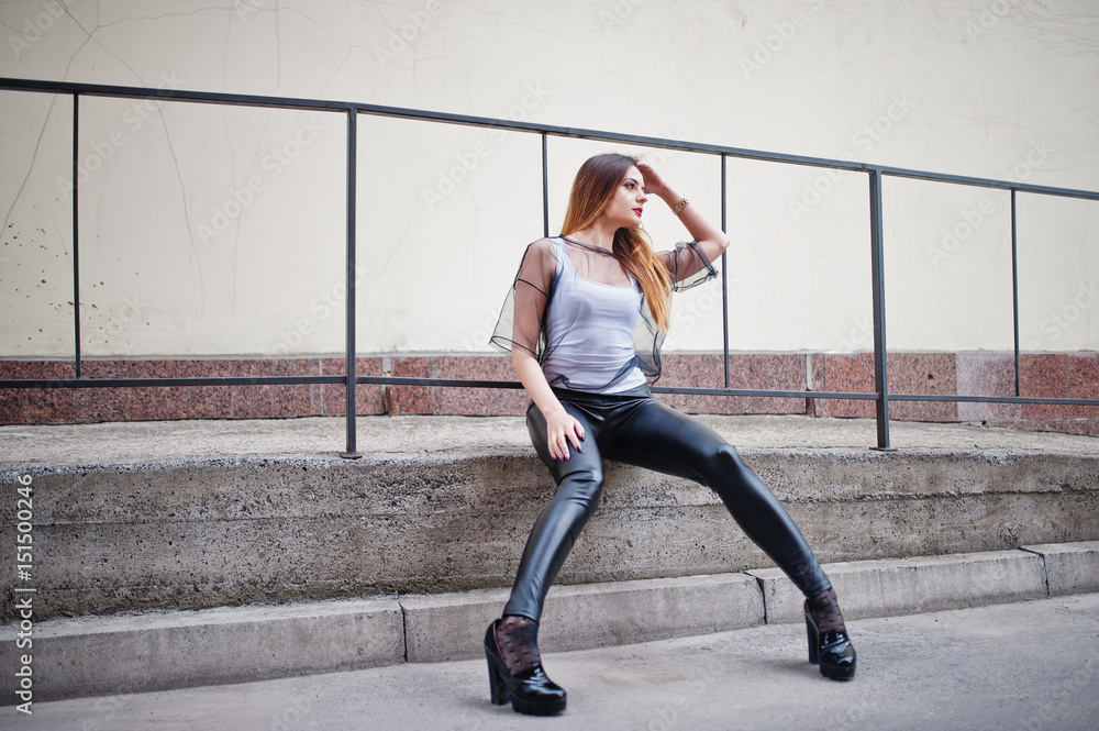 Fashionable woman look at white shirt, black transparent clothes, leather pants, posing at street against iron railings. Concept of fashion girl.