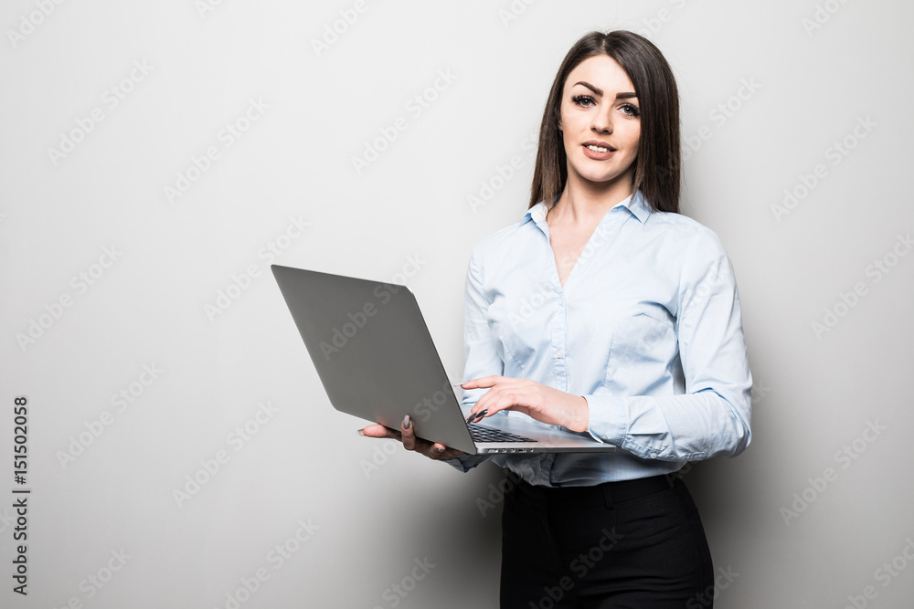 Attractive young girl in casual clothes is holding a laptop, looking at camera and smiling, on gray background Attractive young girl in casual clothes is holding a laptop, looking at camera and smiling, on gray background