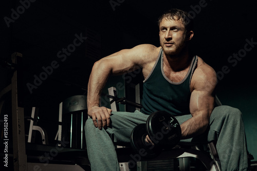 Young athlete jumping, posing with dumbbells in the gym showing a pumped bicep. Bodybuilder