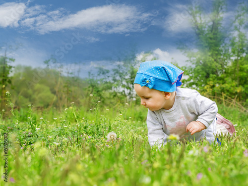 Little cute baby playing on the green flowering meadow