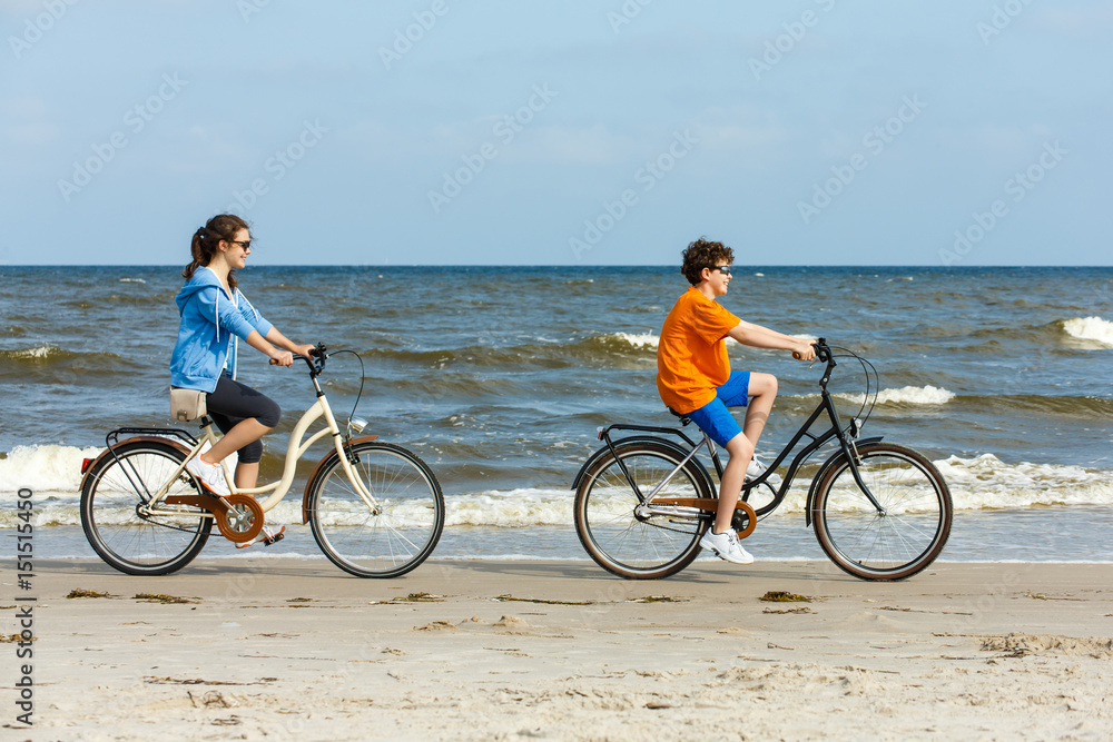 Fototapeta premium Teenage girl and boy biking on beach