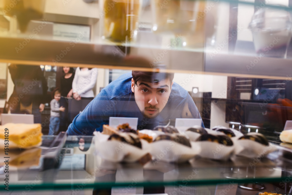 A young guy with interest peeps into the showcase with cakes