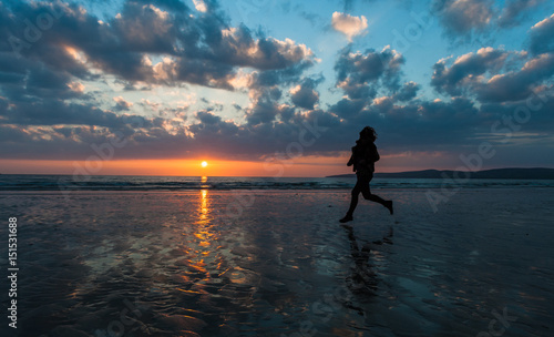 Silhouette of woman running on the beach at sunset 