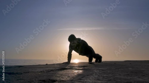 Young athletic man doing gymnastics on the sea early in the morning