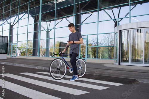  Man with a fixie bicycle walking on the road. young hipster with retro bicycle walking on the crosswalk and texting on the cellphone