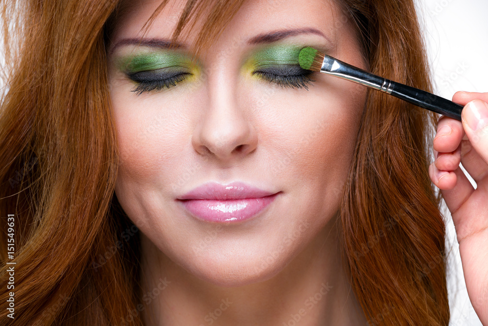 Beautiful sensual red-haired woman. Makeup artist performs makeup on woman's face. Beautiful sensual red-haired woman. Makeup artist performs makeup on woman's face.