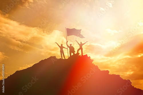 High achiever  silhouettes of three people holding on top of a mountain to raise their hands up. A man on top of a mountain. Conceptual design. Against a dramatic sky with clouds at sunset.