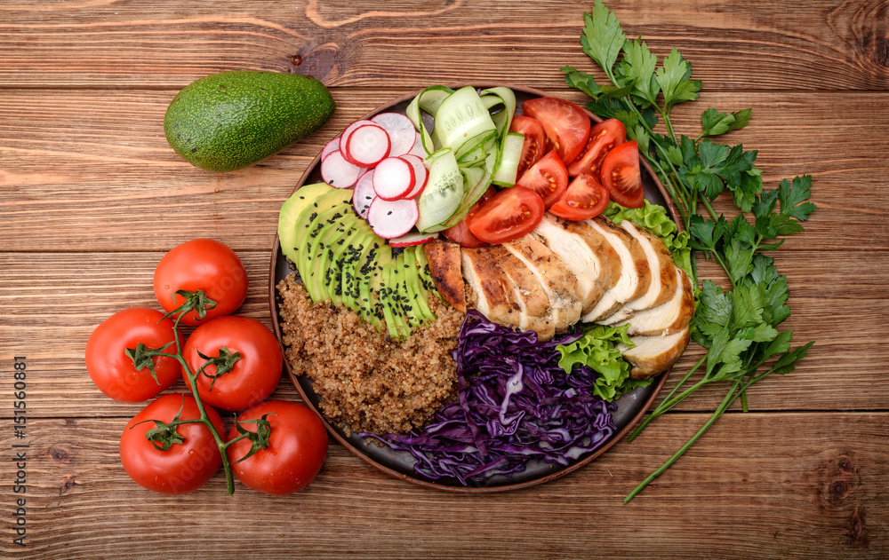 Healthy salad bowl with quinoa, chicken, avocado and vegetables on wooden background .