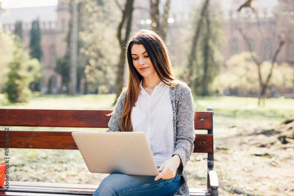 Student Girl using a laptop on a bench in park near campus Student Girl using a laptop on a bench in park near campus