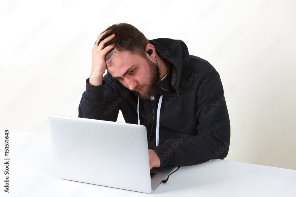 The programmer worried. Works behind the laptop. Isolated, one person on a white background. The programmer worried. Works behind the laptop. Isolated, one person on a white background.