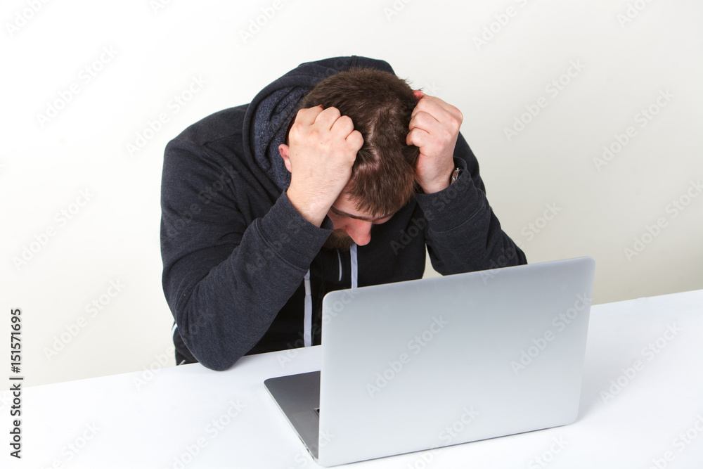 The programmer worried. Works behind the laptop. Isolated, one person on a white background. The programmer worried. Works behind the laptop. Isolated, one person on a white background.