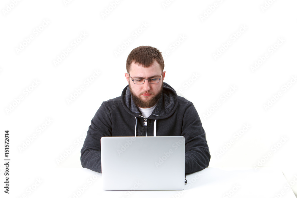 The programmer with glasses works behind the laptop. Isolated, one person on a white background. He is calm. The programmer with glasses works behind the laptop. Isolated, one person on a white background. He is calm.