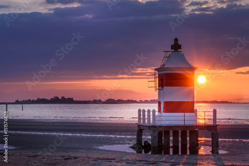 Beautiful sunrise at the seaside in Italy, at Lignano Sabbiadoro, with pier and lighthouse in the foreground.