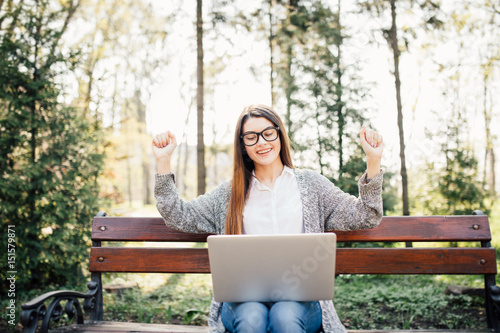 pretty successful woman with her hands raised while working on laptop, outdoor in park bench photo