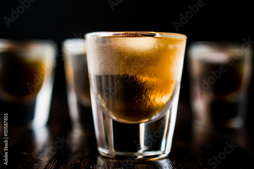 Whiskey Shots with ice on dark wooden surface.