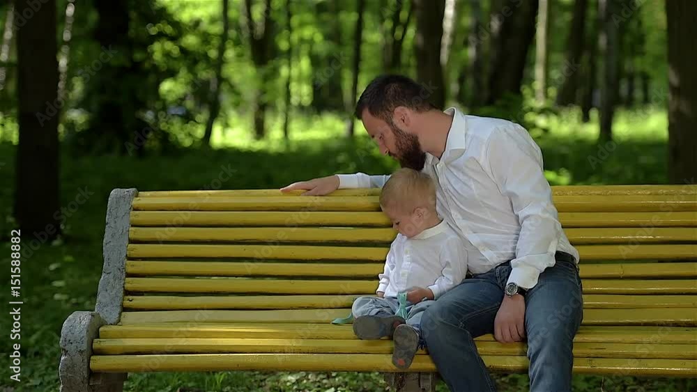 Little boy with his dad are playing with bow tie. They are sitting on a park bench. Father's day. Little boy with his dad are playing with bow tie. They are sitting on a park bench. Father's day.