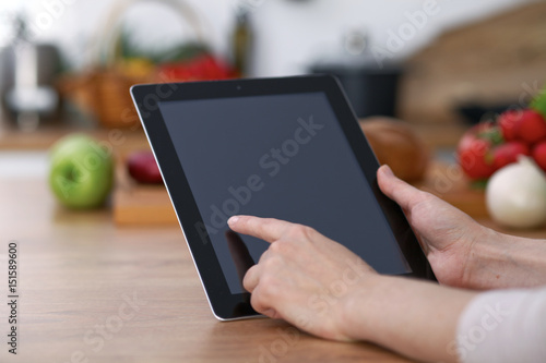Haman hands  using touch pad in the kitchen. Closeup of woman making online shopping by tablet computer and credit card.  Cooking and shopping concept. 