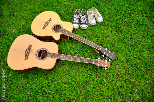 Two guitars and two pairs of shoes on bright green grass texture photo