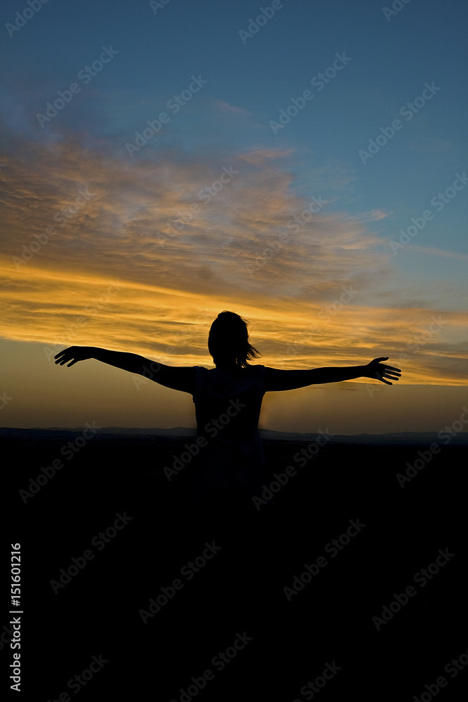 Girl in nature opens her arms during sunset.