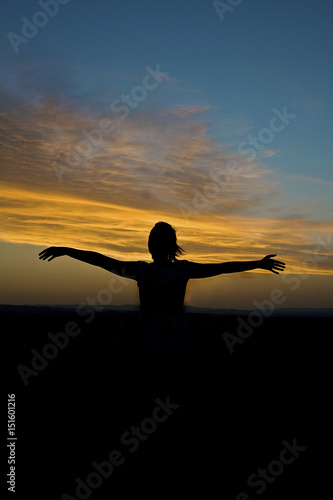 Girl in nature opens her arms during sunset.