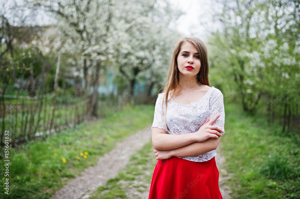 Portrait of beautiful girl with red lips at spring blossom garden, wear on red dress and white blouse.