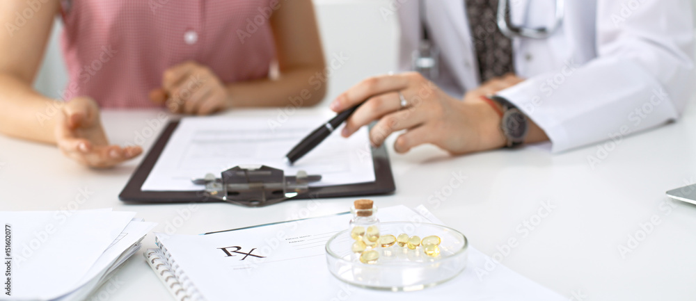 Fototapeta premium Medical prescription form, capsules and pills are lying against the background of a doctor and patient discussing health exam results