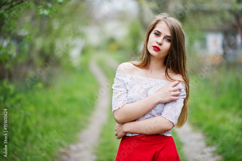 Fototapeta Naklejka Na Ścianę i Meble -  Portrait of beautiful girl with red lips at spring blossom garden, wear on red dress and white blouse.